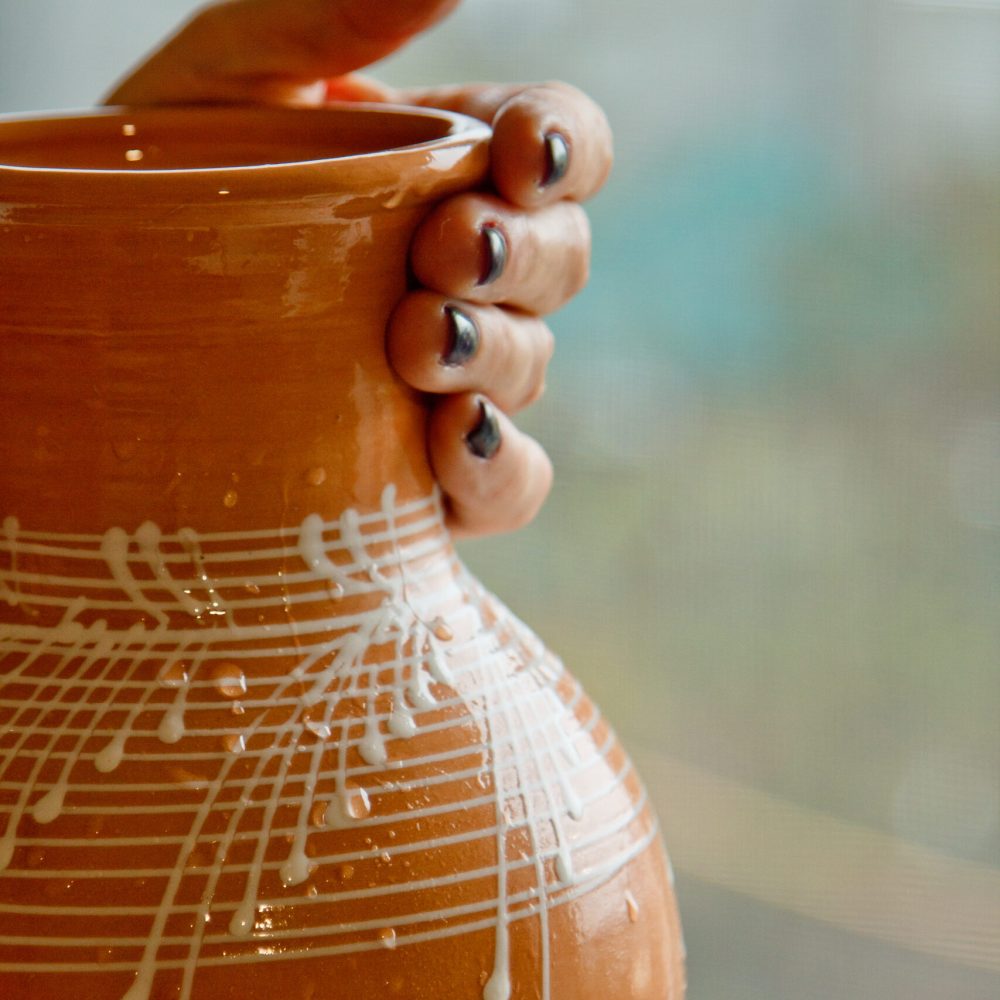 painted with white enamel earthenware jug in female hands. ceramic dishes on a blurred background close up. vertical.